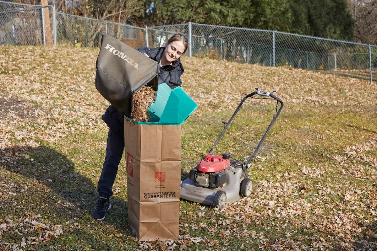 Woman dumps lawn mower leaf collecting bag into a brown yard refuse bag.