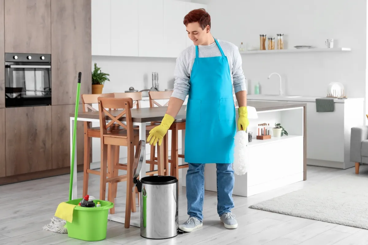 A young man with cleaning supplies is looking to clean the indoor trash can.