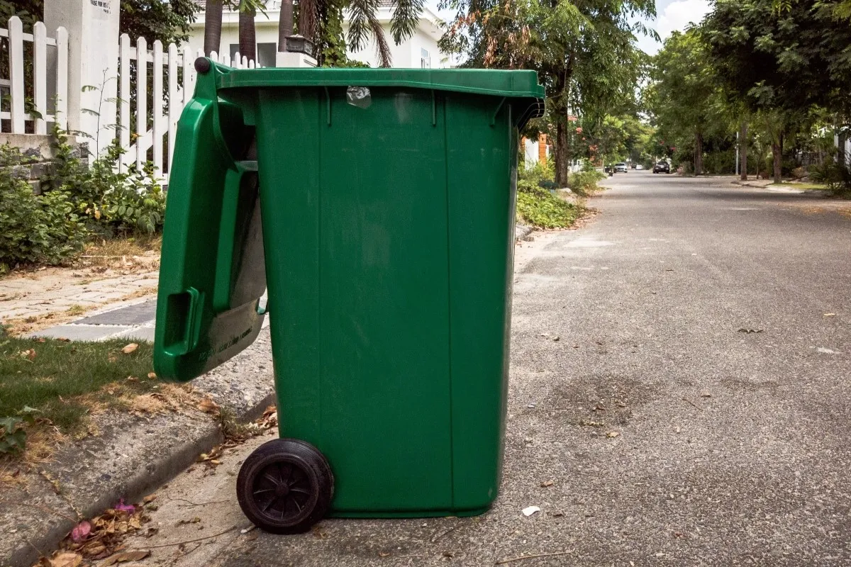 A green opened empty plastic trash can in front of a home.