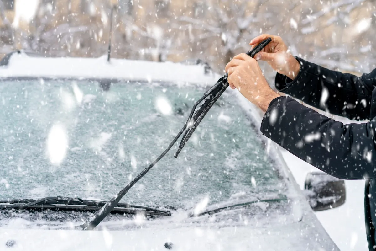A man adjusts his windshield wipers on a snowy winter day.