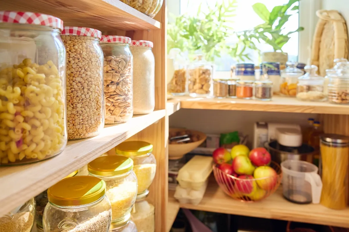 Several canned and jarred non-perishable foods in a tidy kitchen pantry.