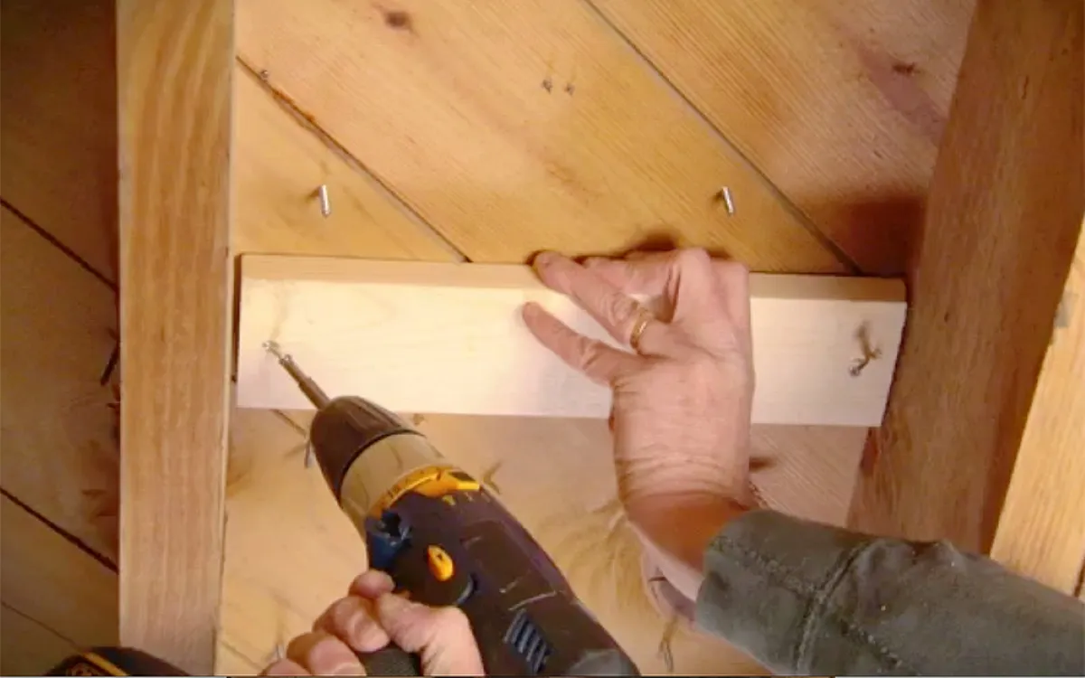 Person screws a block of wood into some floor joists.