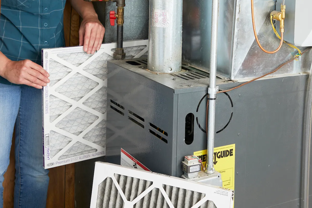 Woman inserts a new filter into a furnace, the old one propped up in front.