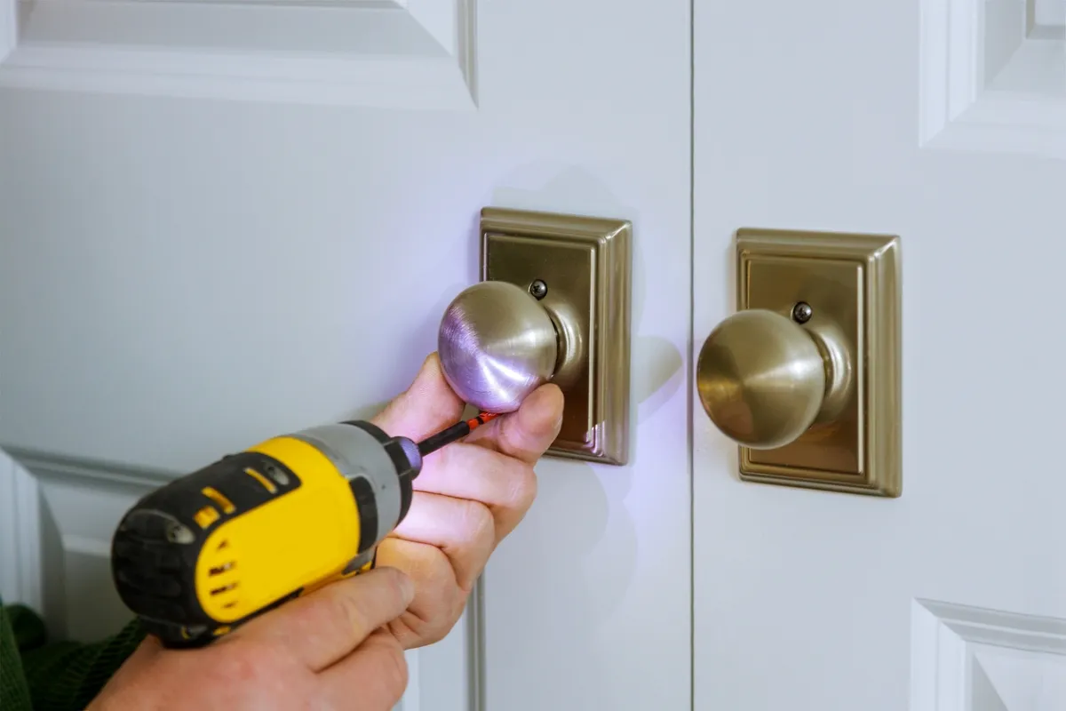 Person uses an electric screwdriver on an indoor doorknob set.
