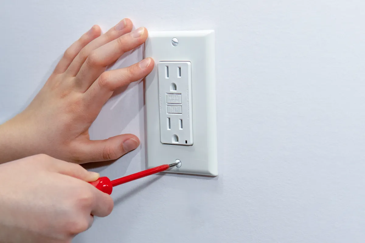 Attaching a white outlet cover to an electrical wall outlet