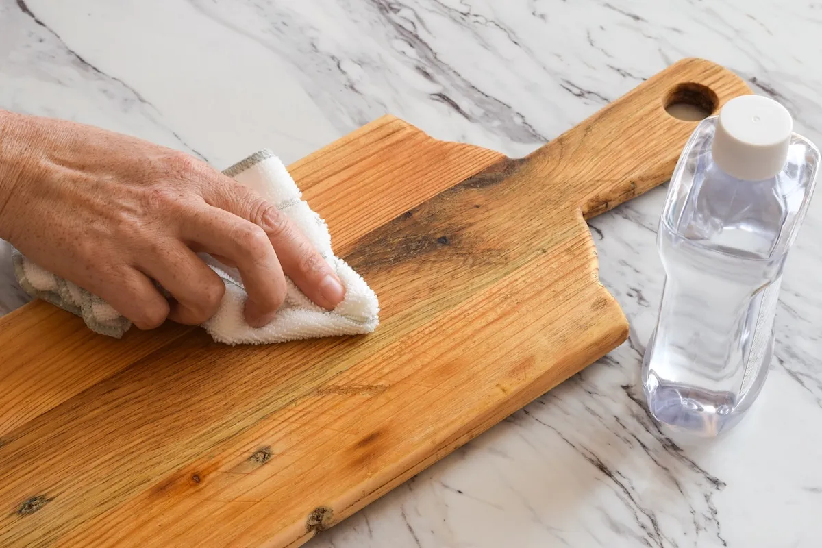 Closeup of a hand treating a wooden cutting board with mineral oil.