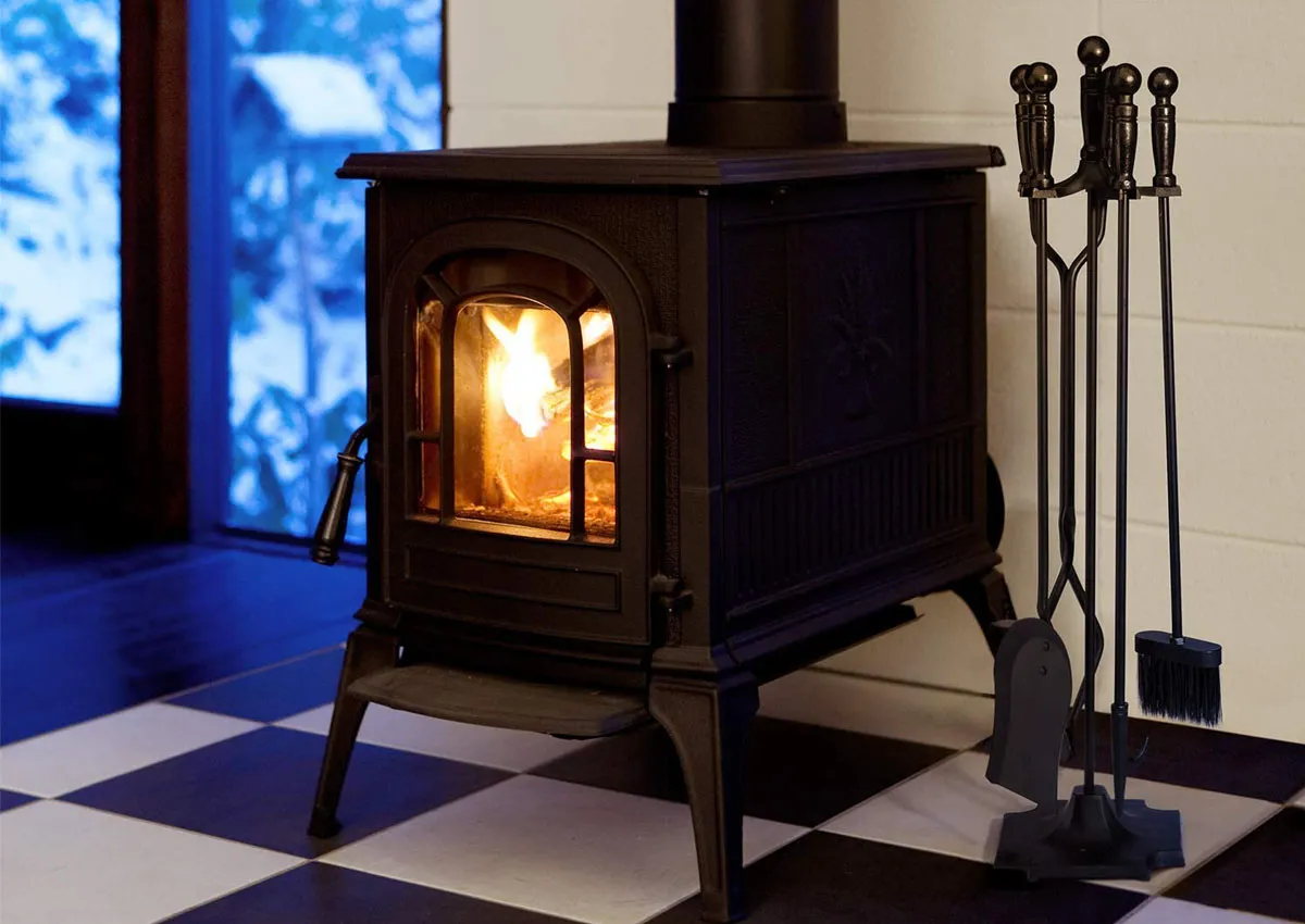 A set of the best fireplace tools next to a small wood-burning stove that's burning a fire.