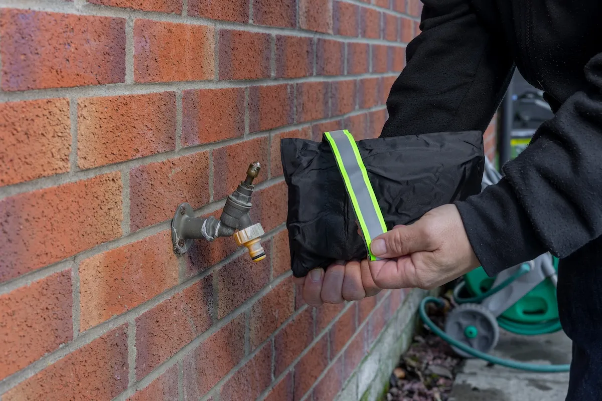 Person installing a frost cover over outdoor spigot to prevent leaks.