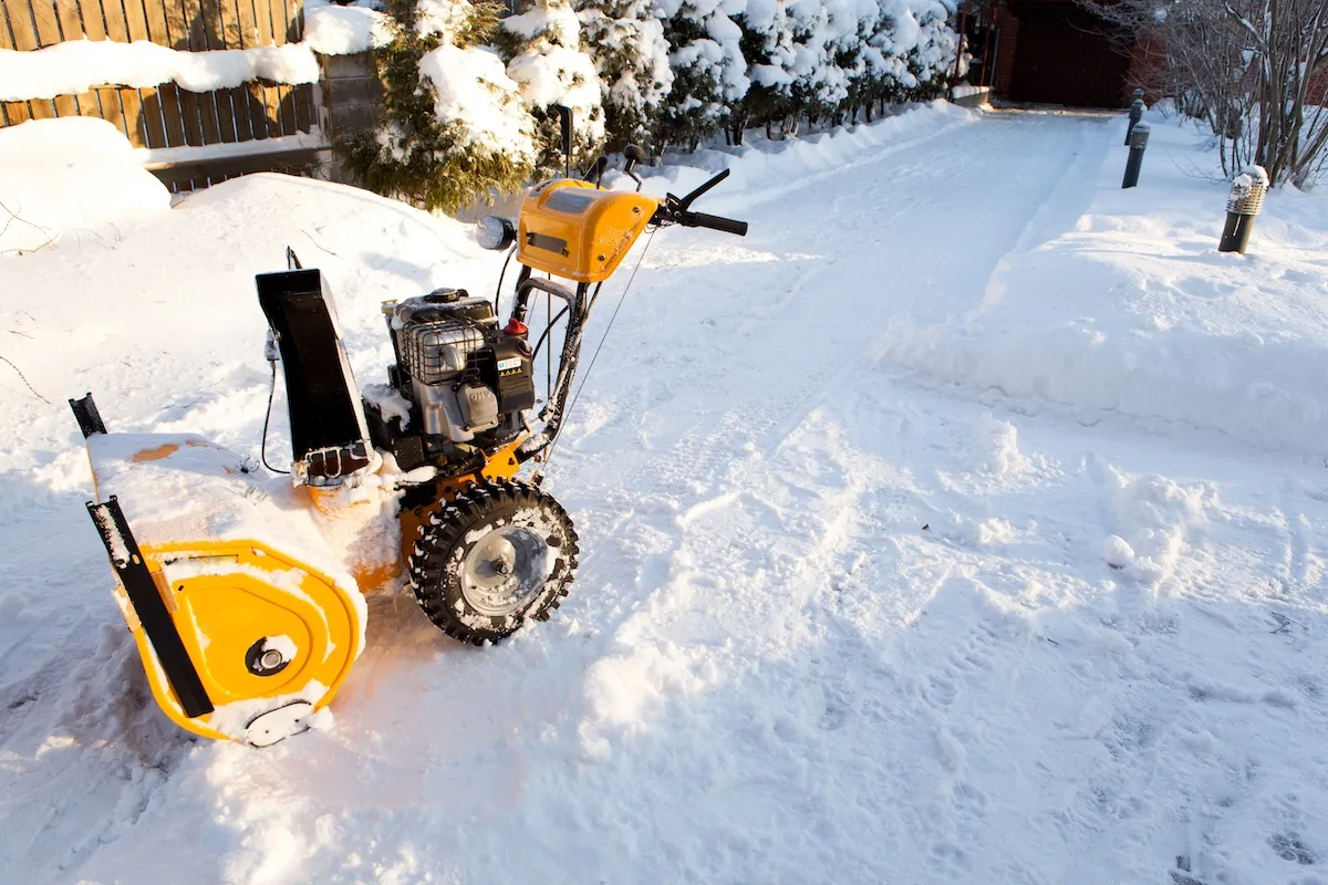 A standing yellow snowblower on a sidewalk.